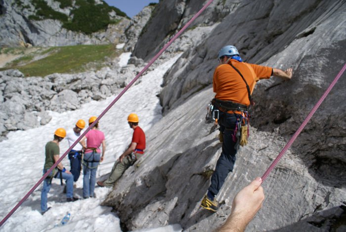 A group climbing a rocky mountain with safety ropes, helmets, and harnesses.