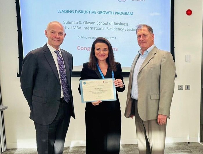 A woman holding a diploma flanked by two men in business suits.