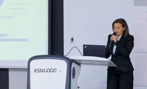 Hala Achkar Slaiby presenting beside a podium with a microphone.
